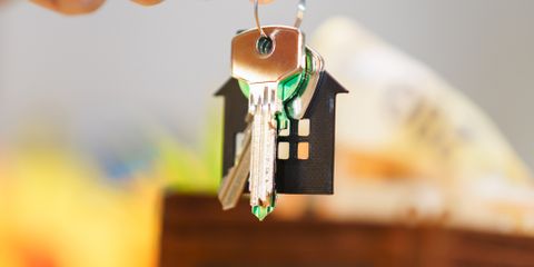 Hand holding house keys representing real estate investment with coins and wallet.
