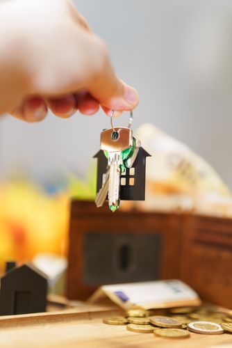 Mano sosteniendo las llaves de la casa que representan una inversión inmobiliaria con monedas y billetera.