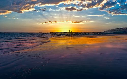 Free Two people walk on a serene beach during sunset with colorful sky reflections. Stock Photo