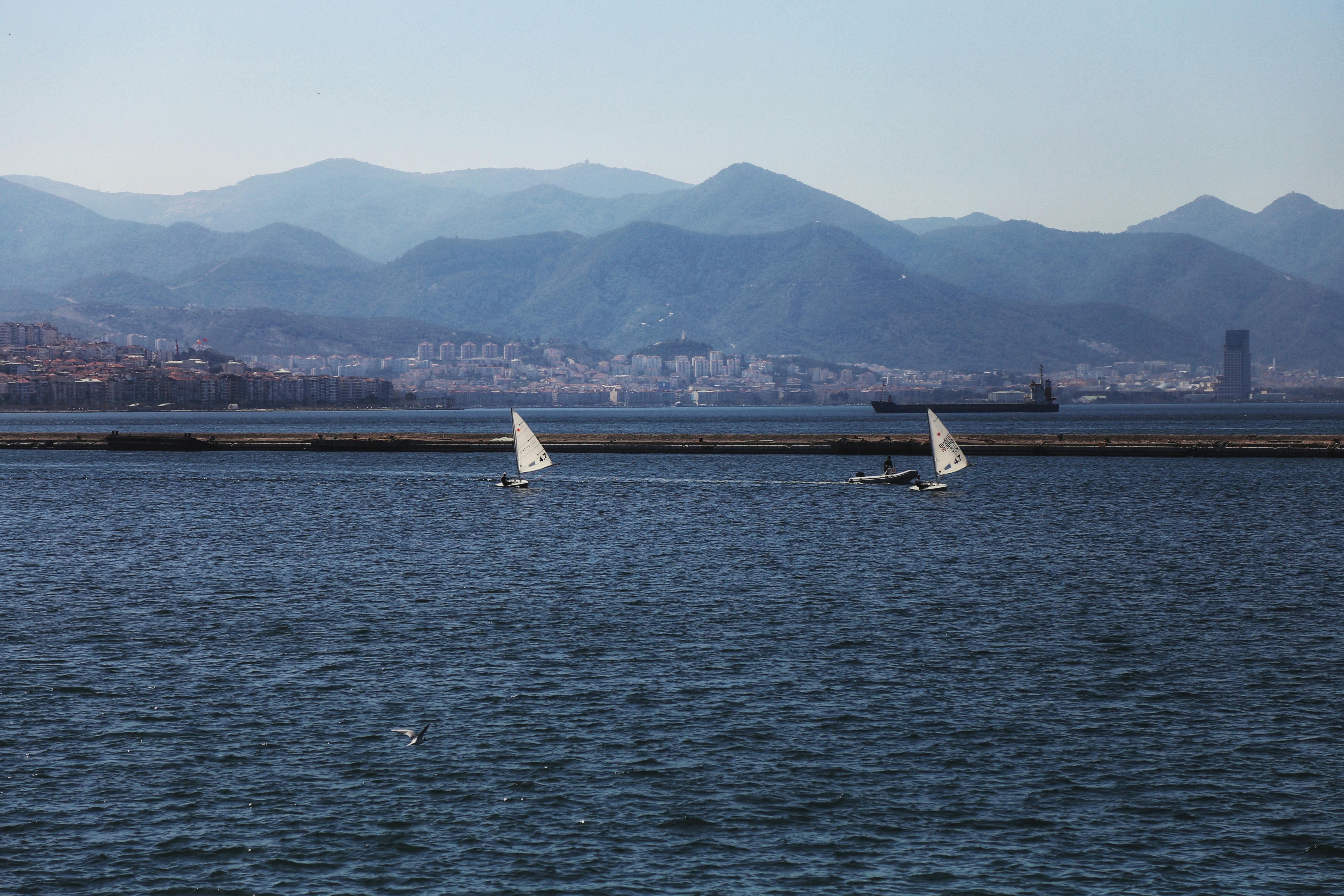 Sailboats navigating the serene Aegean Sea with İzmir's stunning mountainous backdrop.
