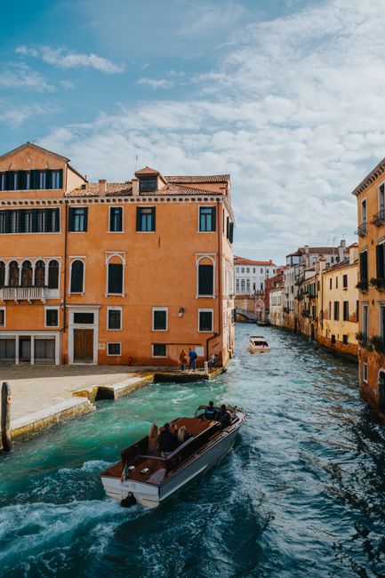 Charming view of Venice canal with boats passing by historic buildings under a clear sky.