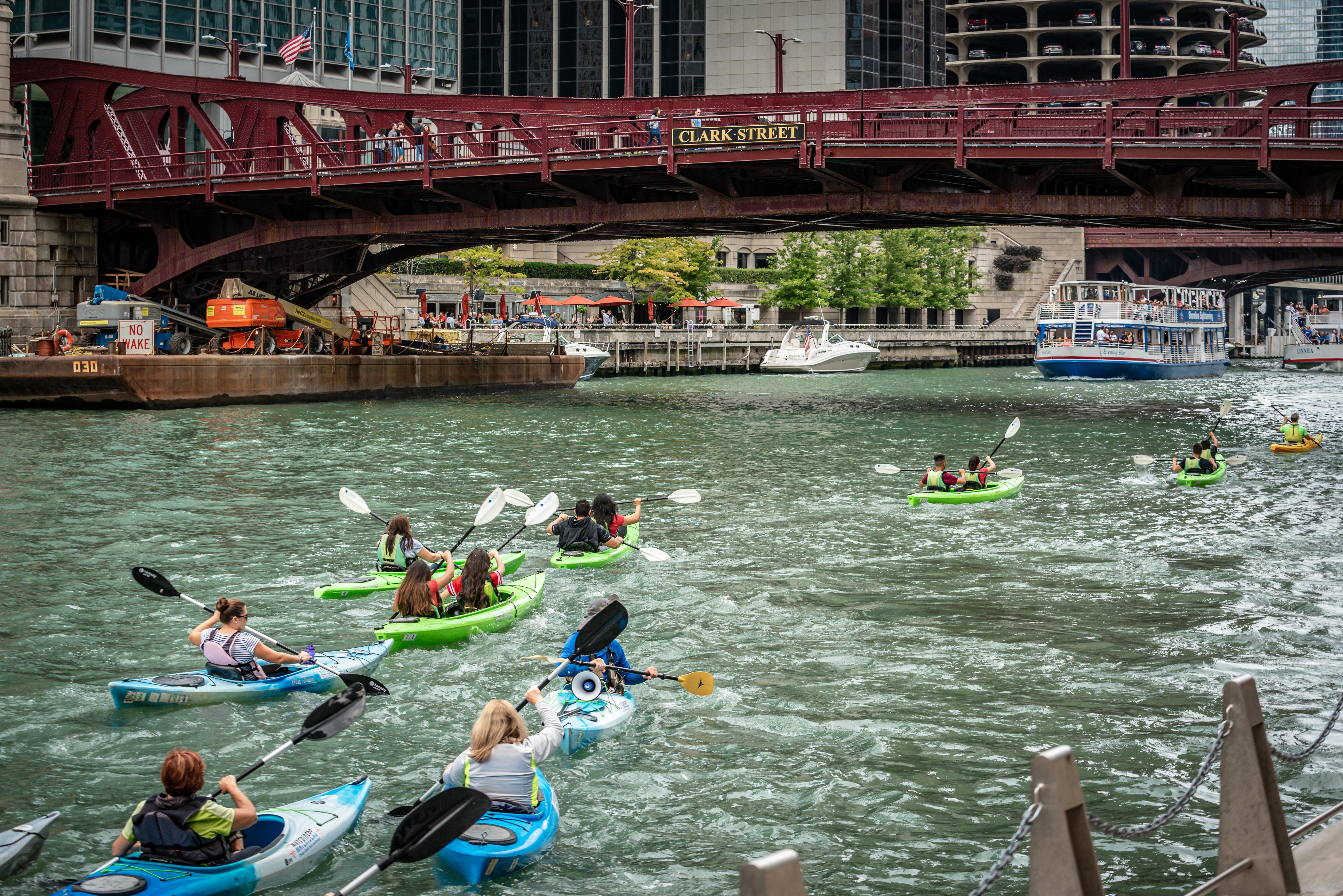 Group of kayakers paddling under Clark Street Bridge in Chicago, showcasing urban outdoor activity.