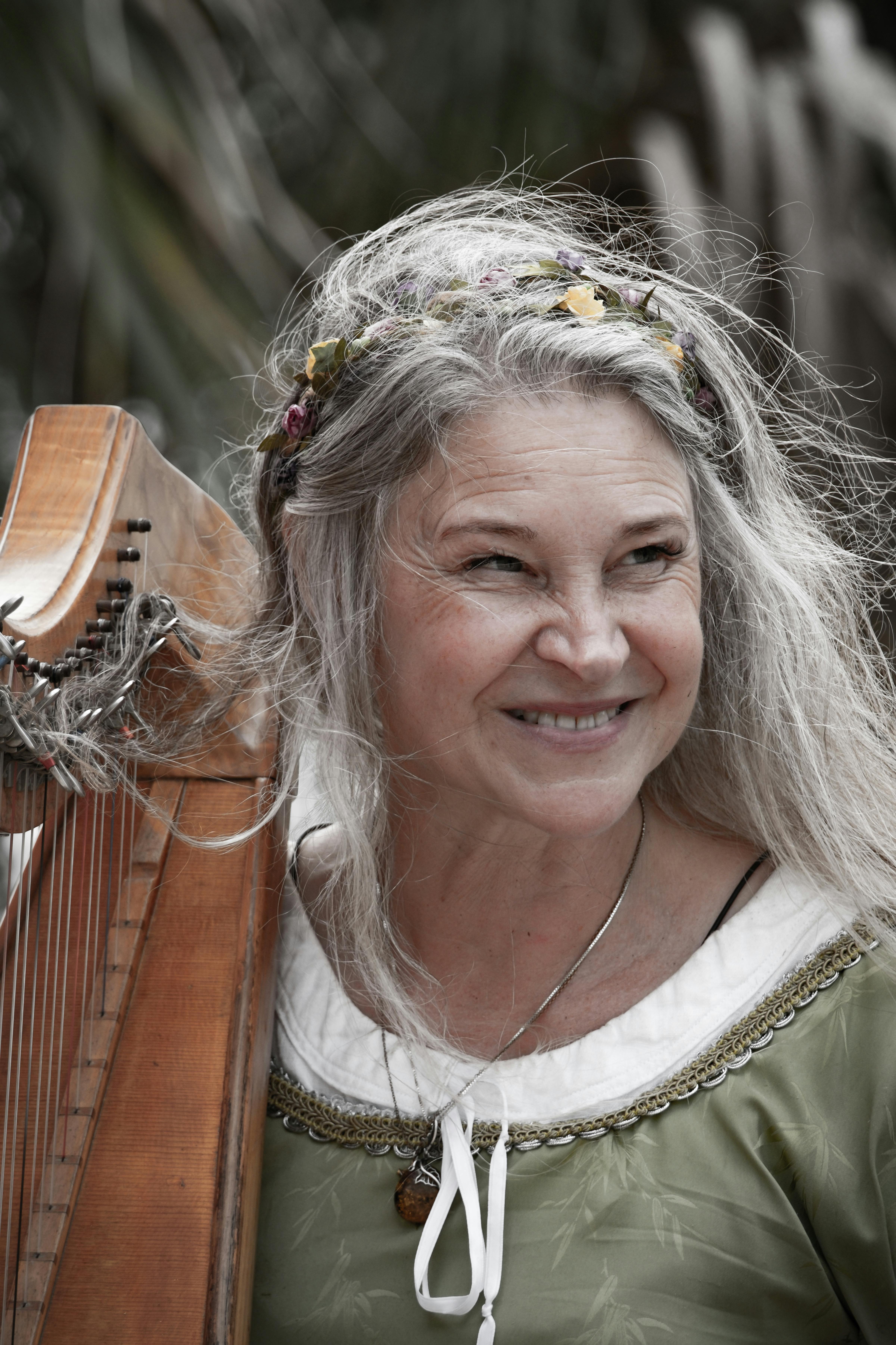 A joyful senior woman with a harp enjoying a festive day outdoors.