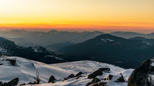 Serene snow-capped mountains under a vibrant sunset sky with layers of distant peaks.