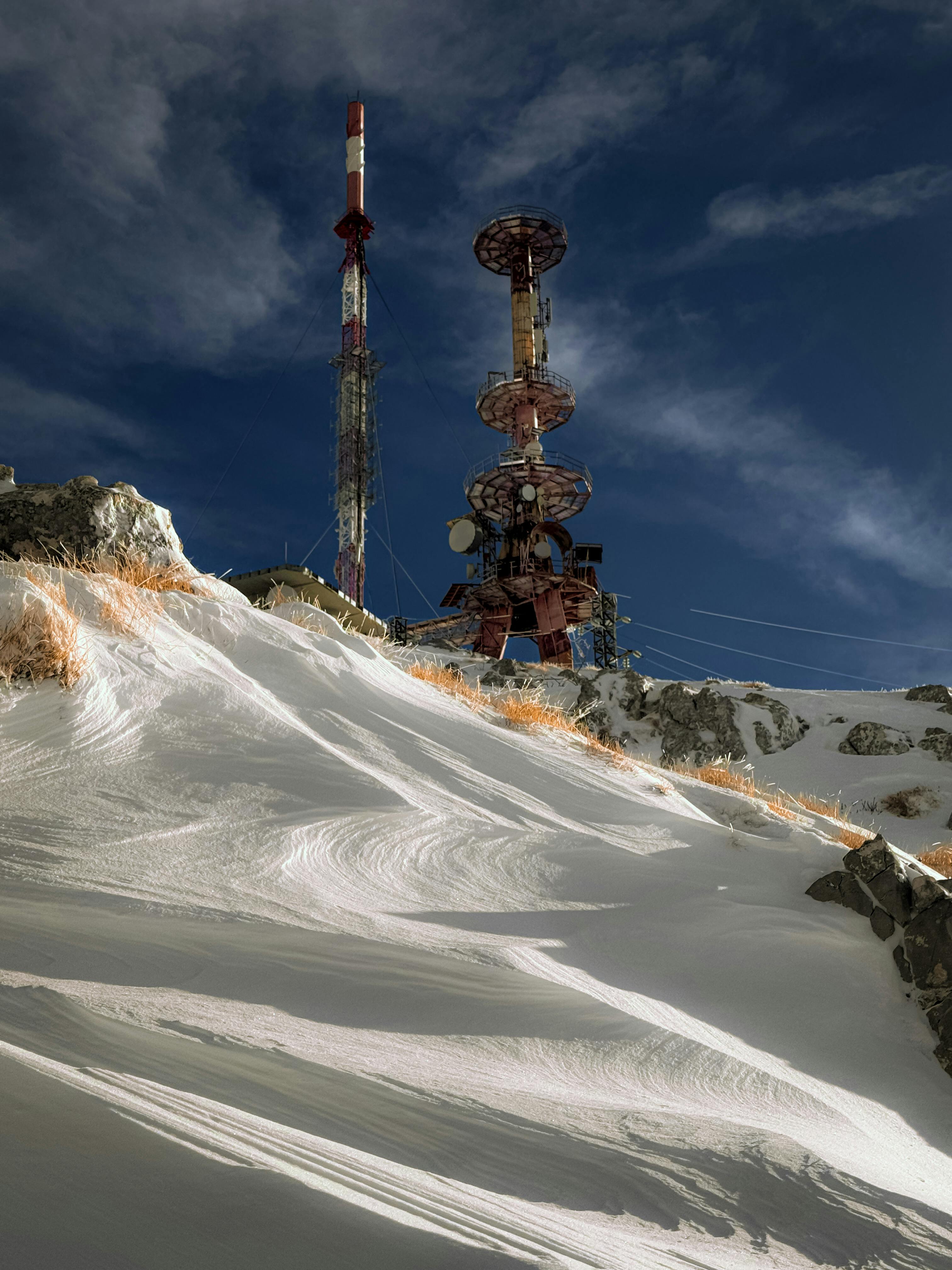 Telecommunication towers standing amid snowy mountain terrain under a clear blue sky.