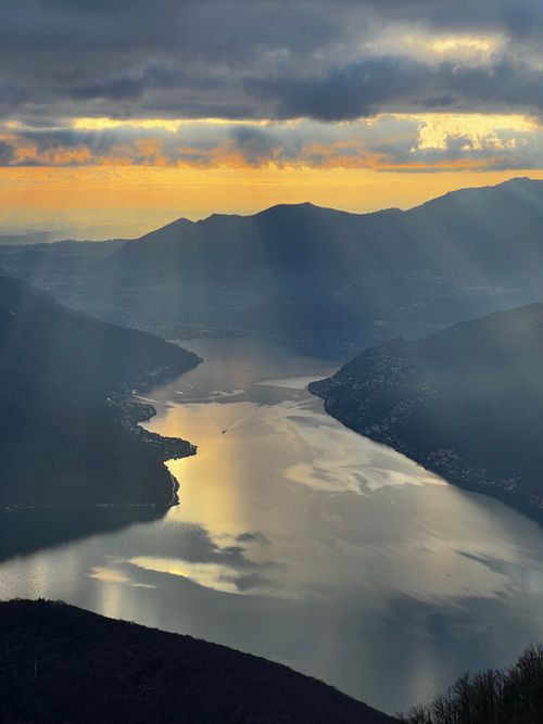 Free Breathtaking aerial view of Lake Lugano with golden sunset rays breaking through clouds. Stock Photo