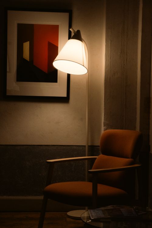 Free Warmly lit cozy corner with an armchair and modern art print on wall. Stock Photo