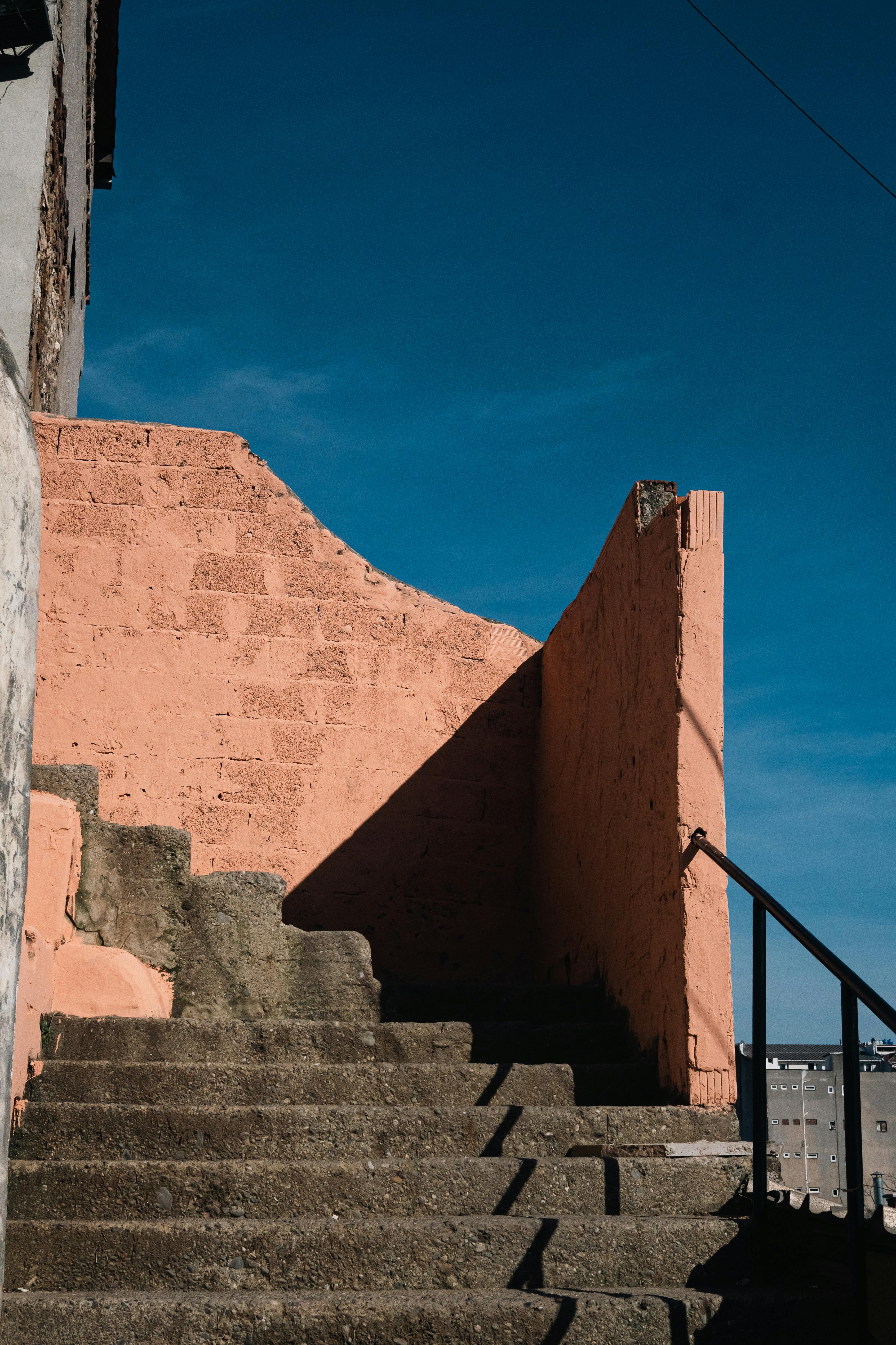 An outdoor staircase with pink walls and blue sky creates a vivid, rustic scene.