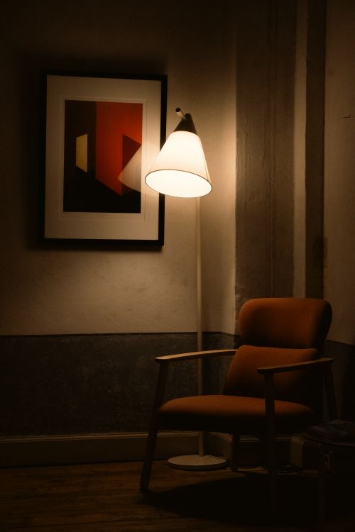 Free A warm, inviting corner featuring a modern armchair, floor lamp, and abstract art. Stock Photo