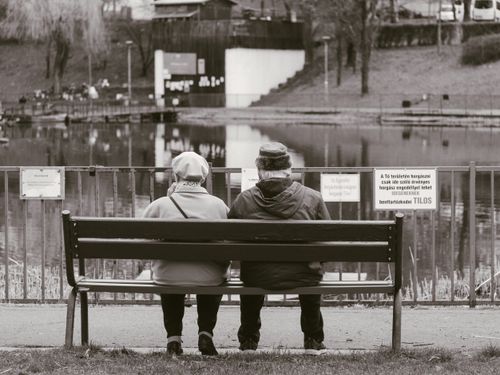 Free A serene scene of an elderly couple sitting on a bench by the lake, captured in black and white. Stock Photo