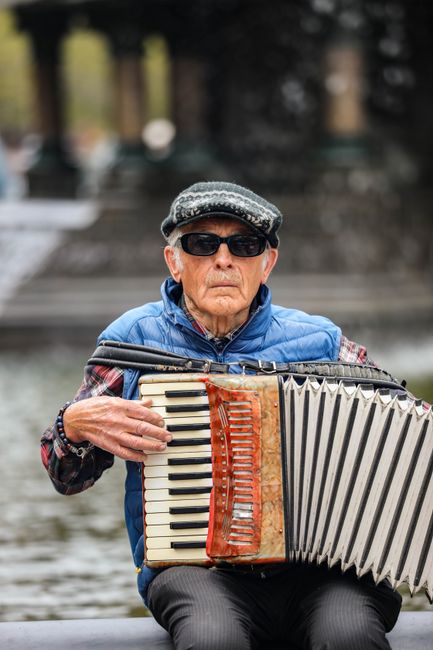 Senior man playing accordion by a fountain in New York City.