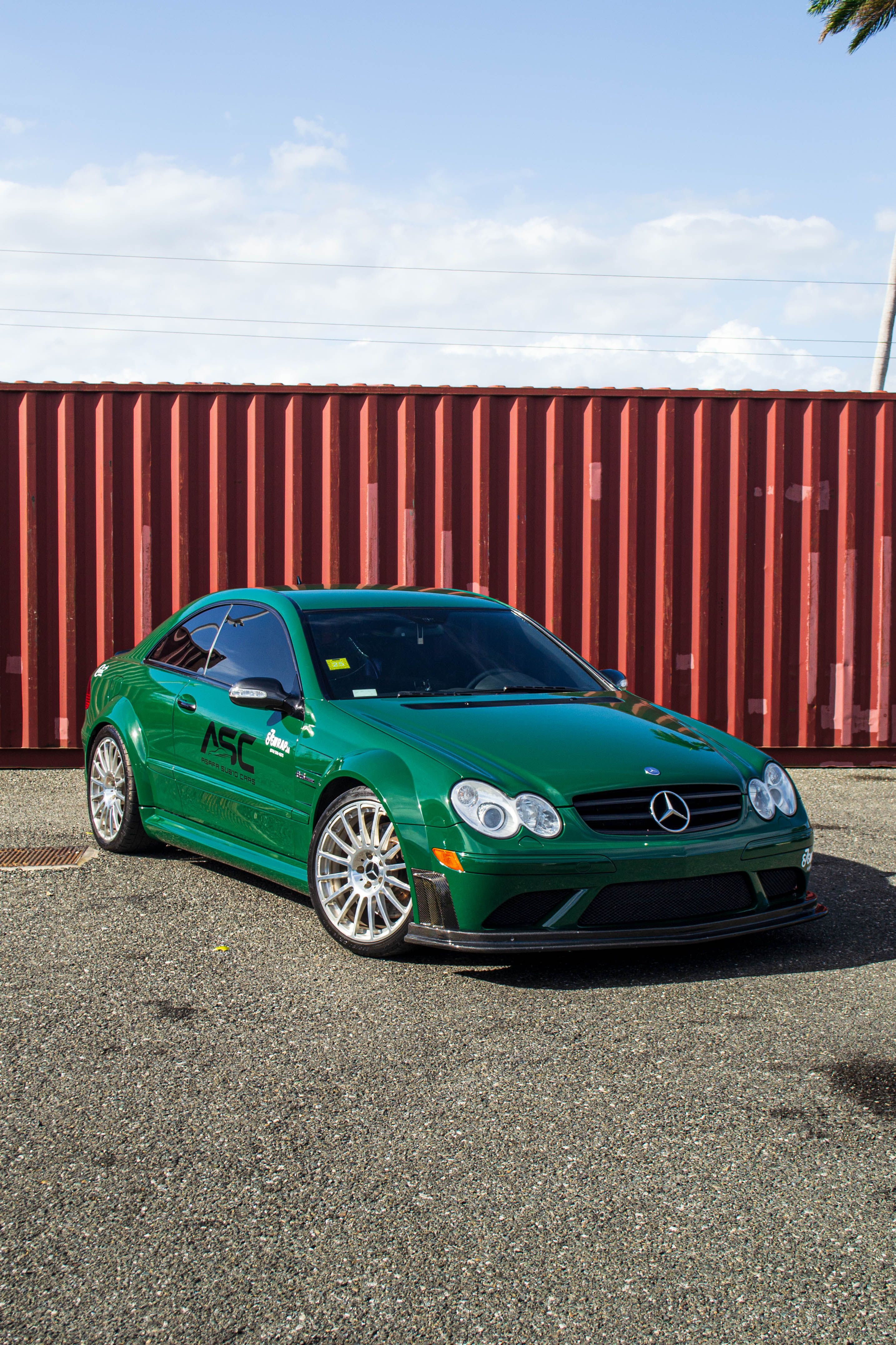 A sleek green sports car parked beside a red shipping container on a sunny day.