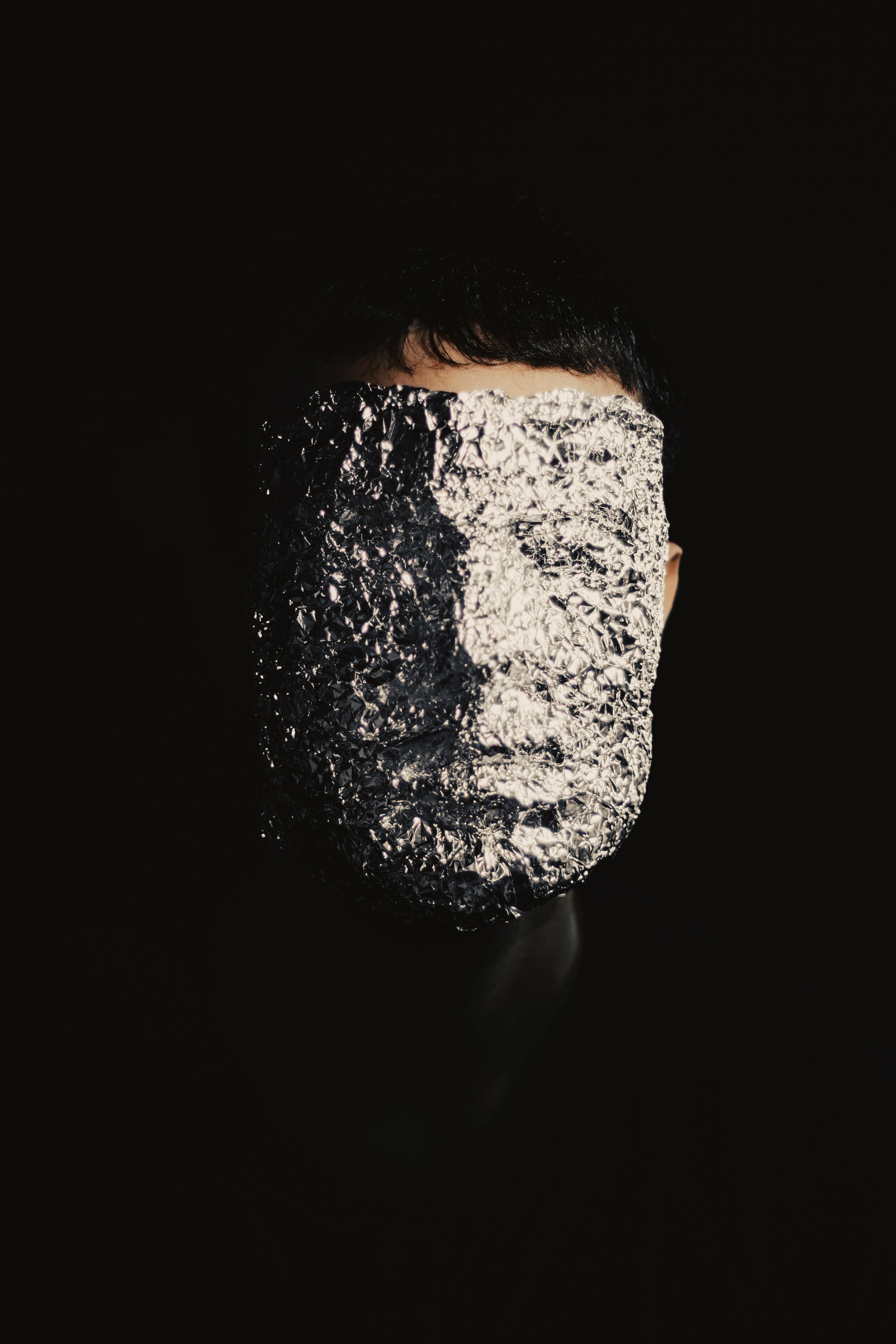 A creative portrait where a person's face is covered with aluminum foil, set against a dark backdrop.