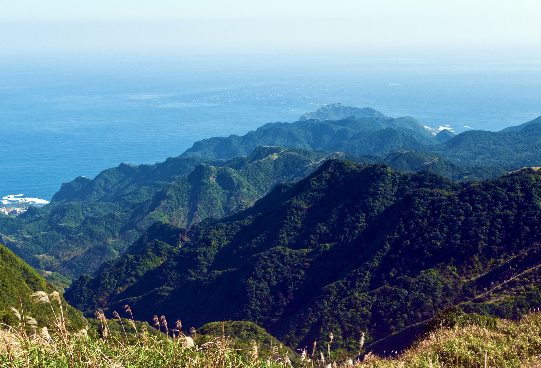 Breathtaking view of lush green mountain range and distant ocean horizon under a bright blue sky.