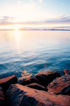 日落时分，海边宁静的景色中，岩石反射着天空温暖的色调