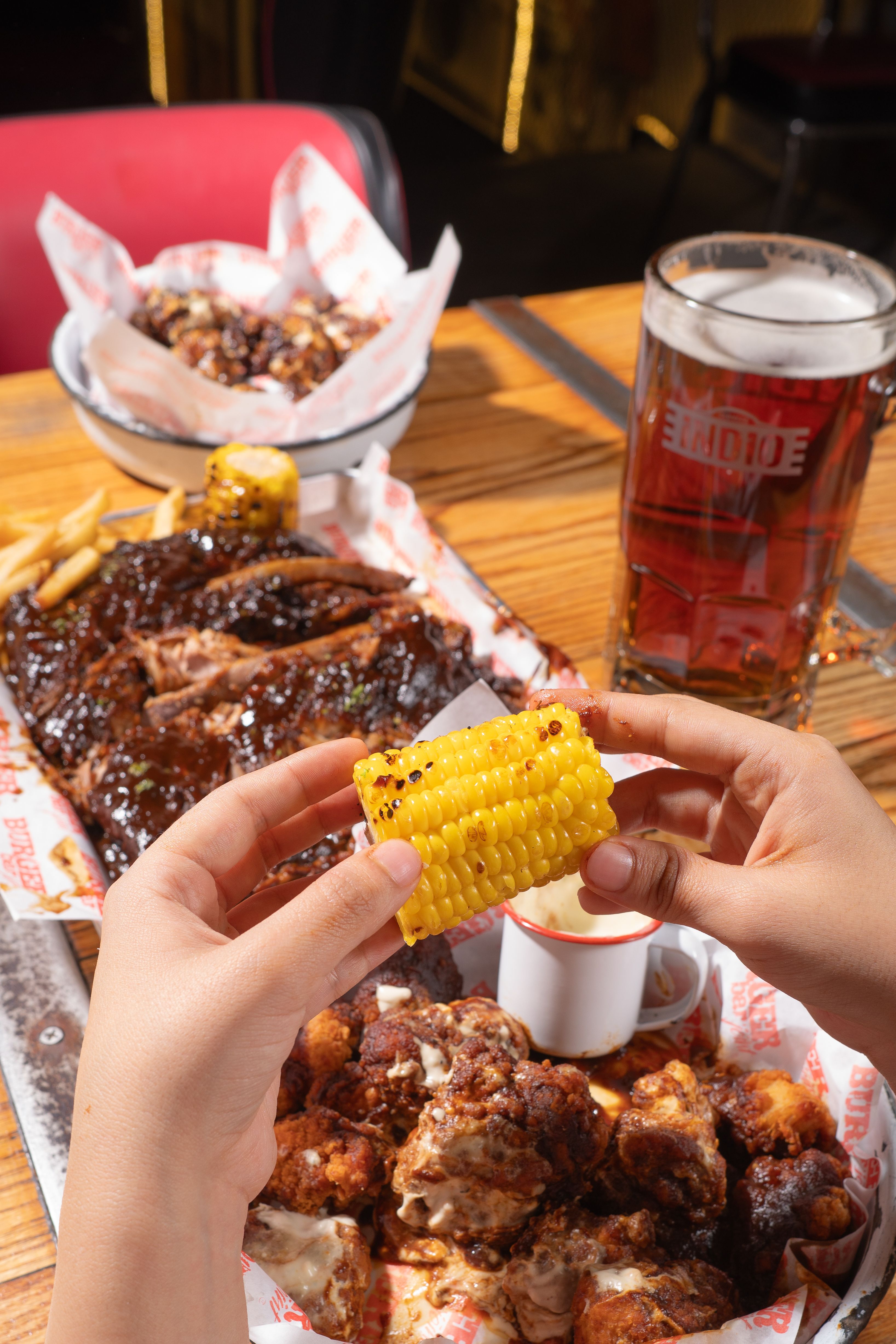 Close-up of grilled corn with barbecue ribs and beer on a wooden table, perfect for a summer meal.