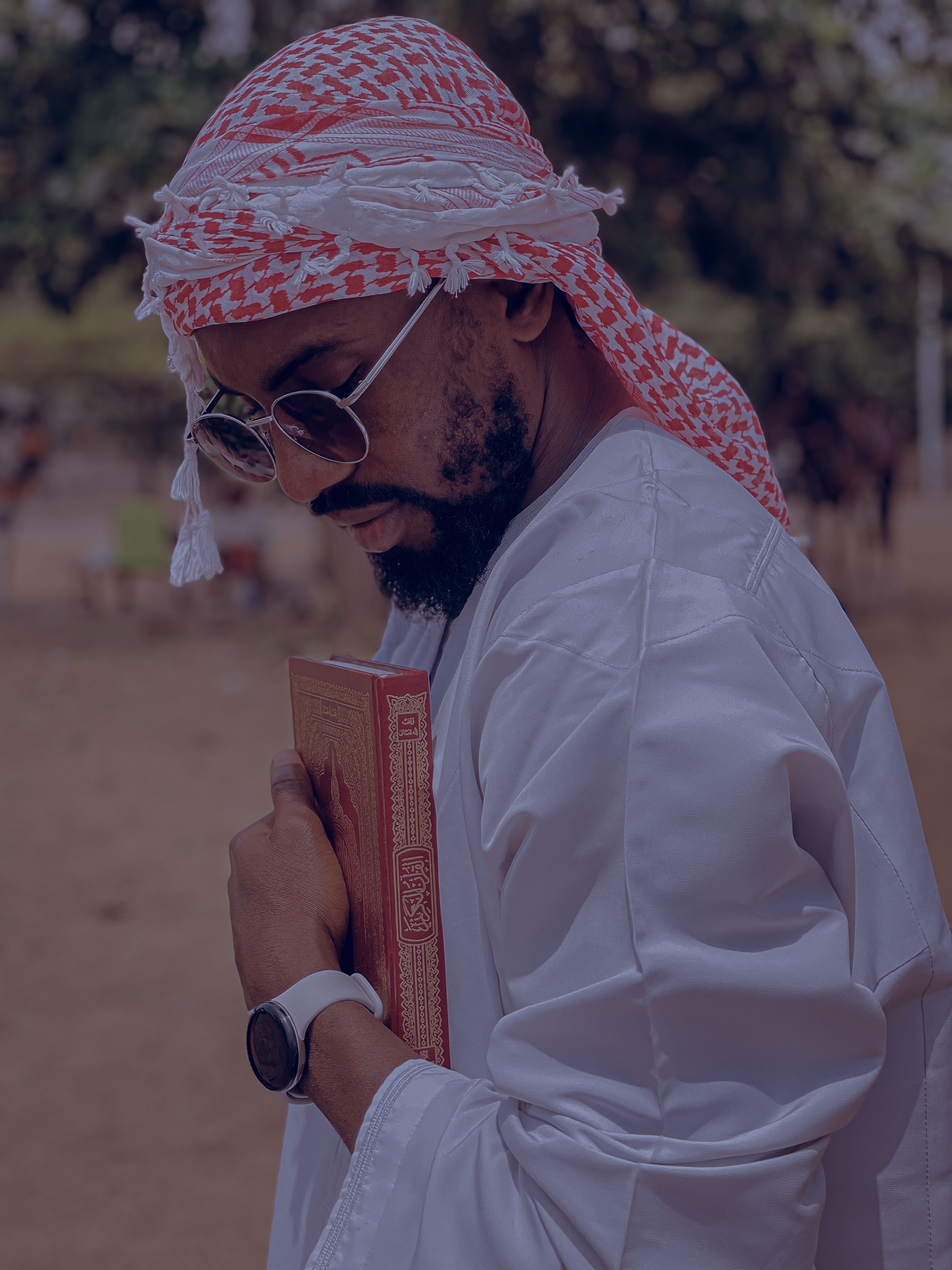 A man in traditional Middle Eastern attire holds a book outdoors, exuding style and cultural essence.