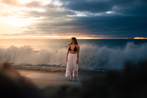 Free A woman stands on the beach at sunset, waves crashing behind her. Stock Photo