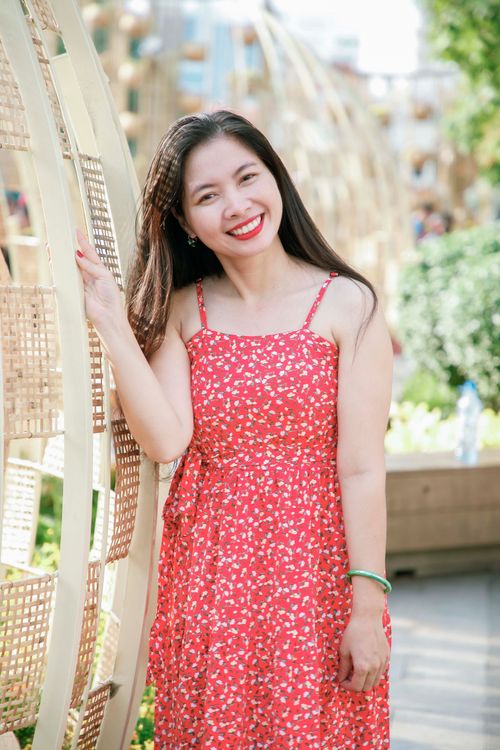 Free Cheerful woman in a red floral dress posing outdoors on a sunny day. Stock Photo