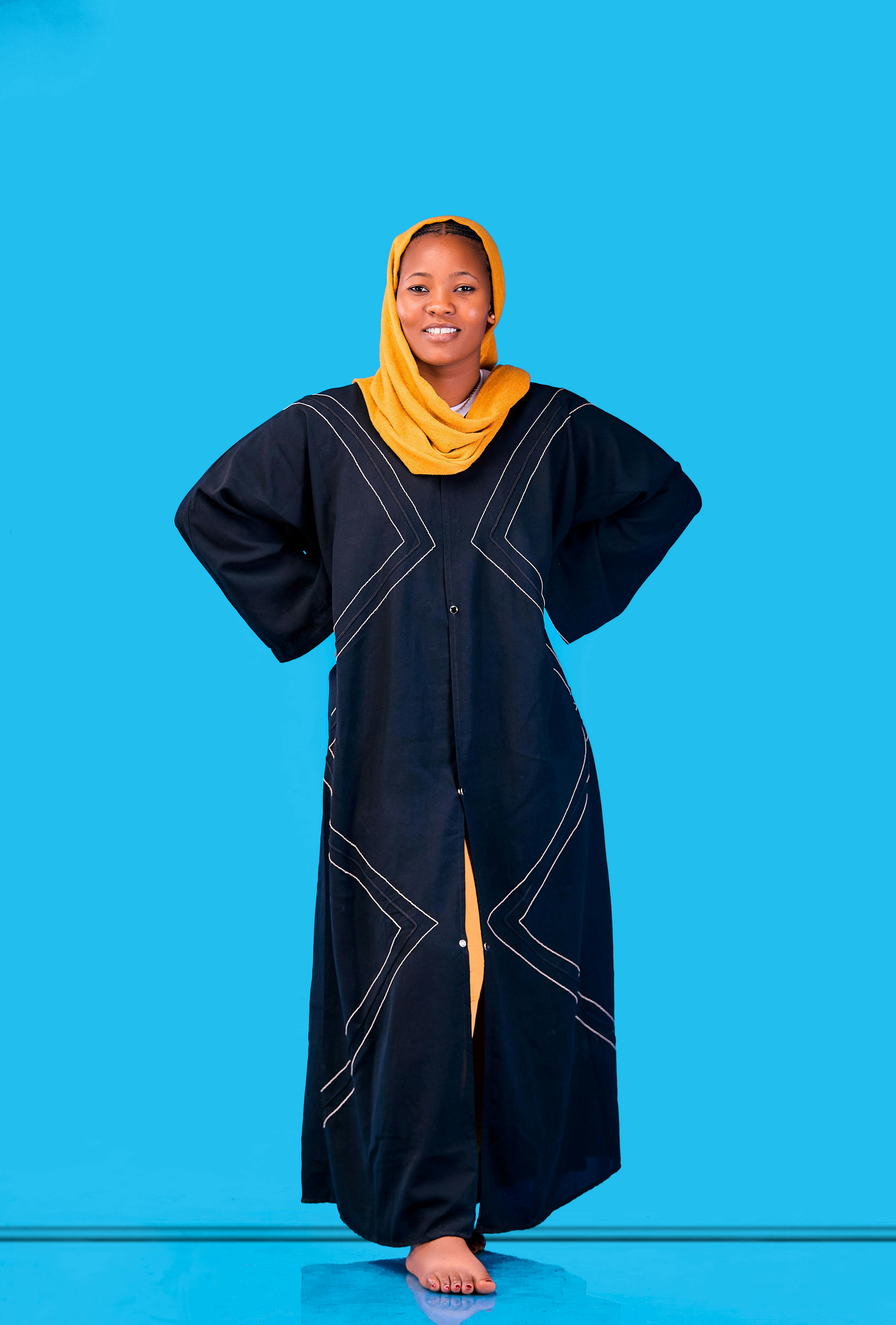 grátis Mulher sorridente usando um vestido preto tradicional com lenço amarelo sobre fundo azul. Foto profissional