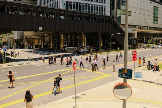 Busy crosswalk scene in a city with people walking and cycling under a bright sky.