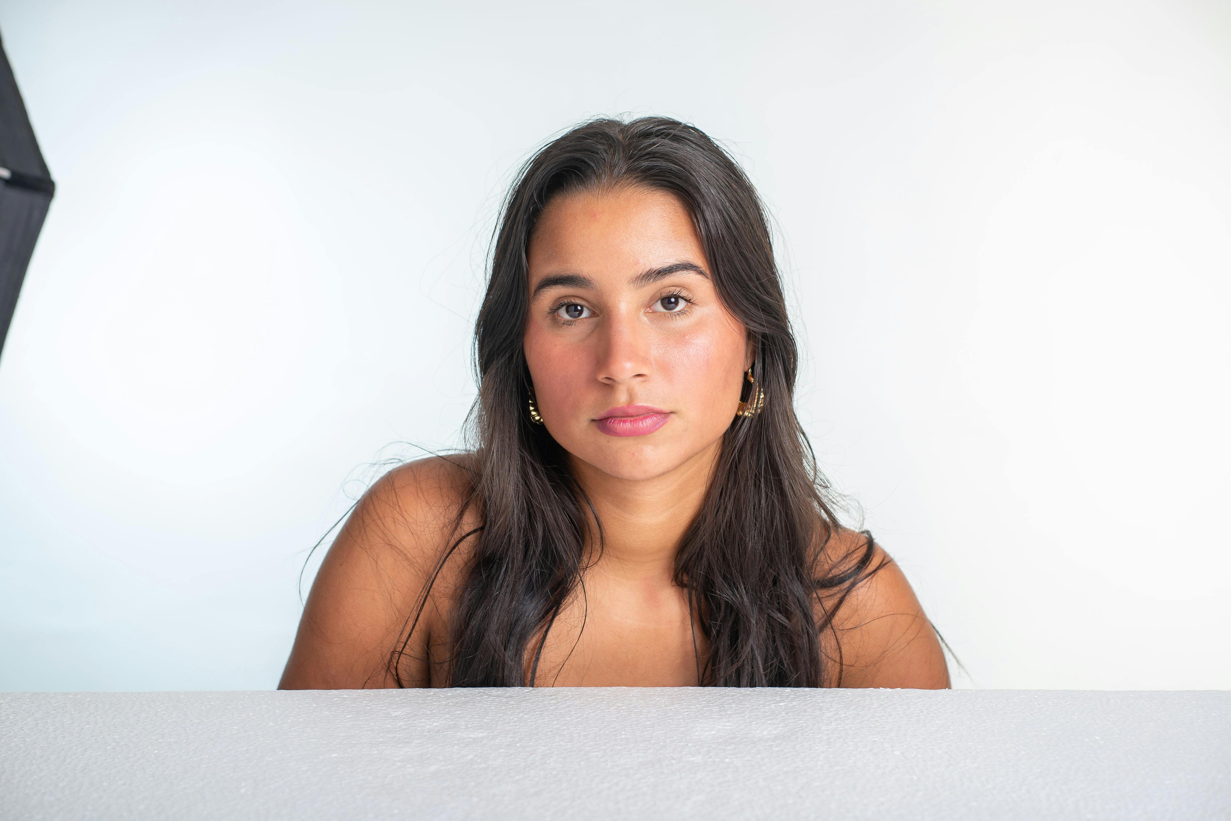 grátis Retrato de uma jovem mulher com longos cabelos escuros sobre um fundo branco. Foto profissional