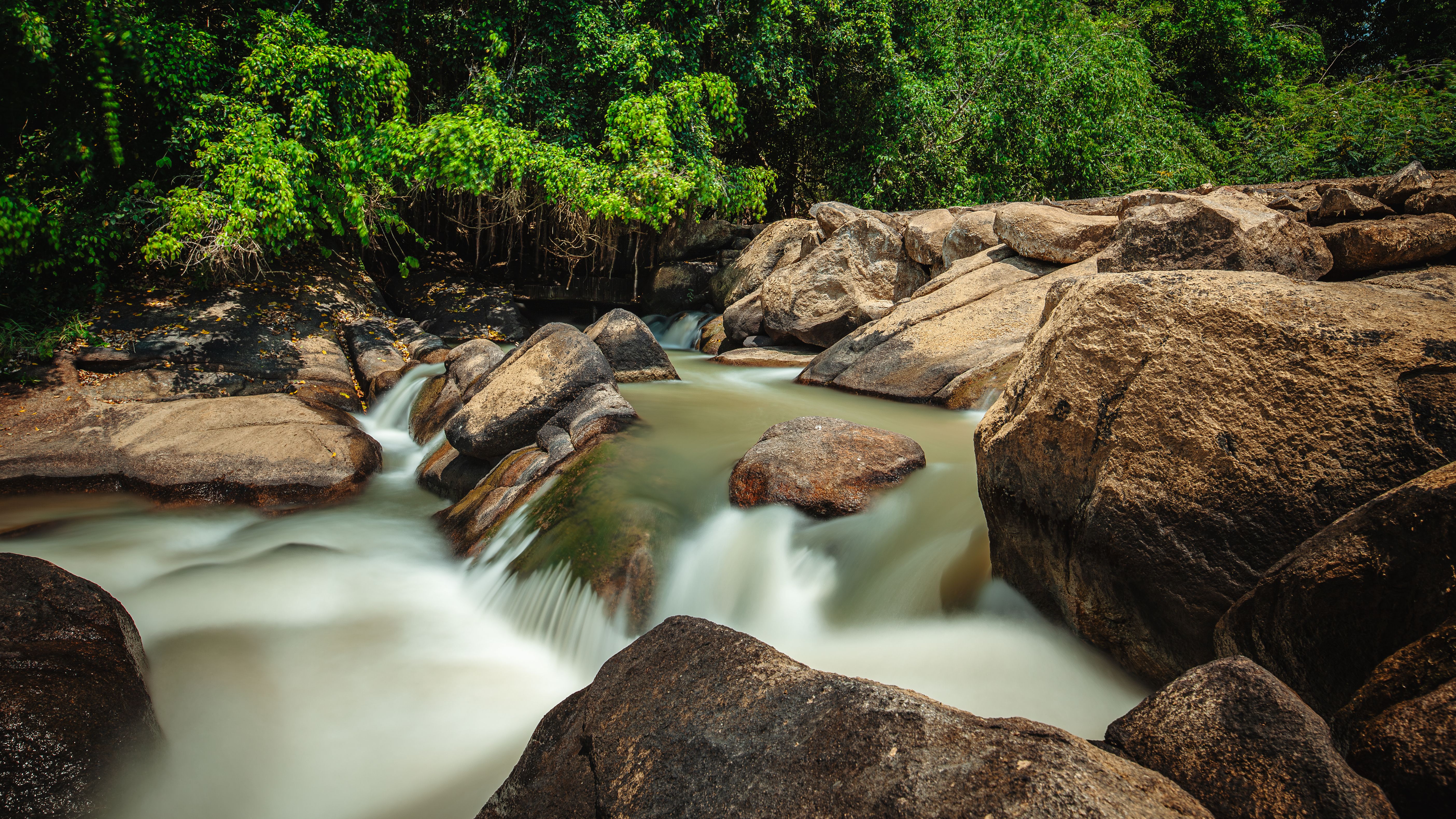 A tranquil scene capturing a waterfall gently flowing through rocks surrounded by lush greenery.