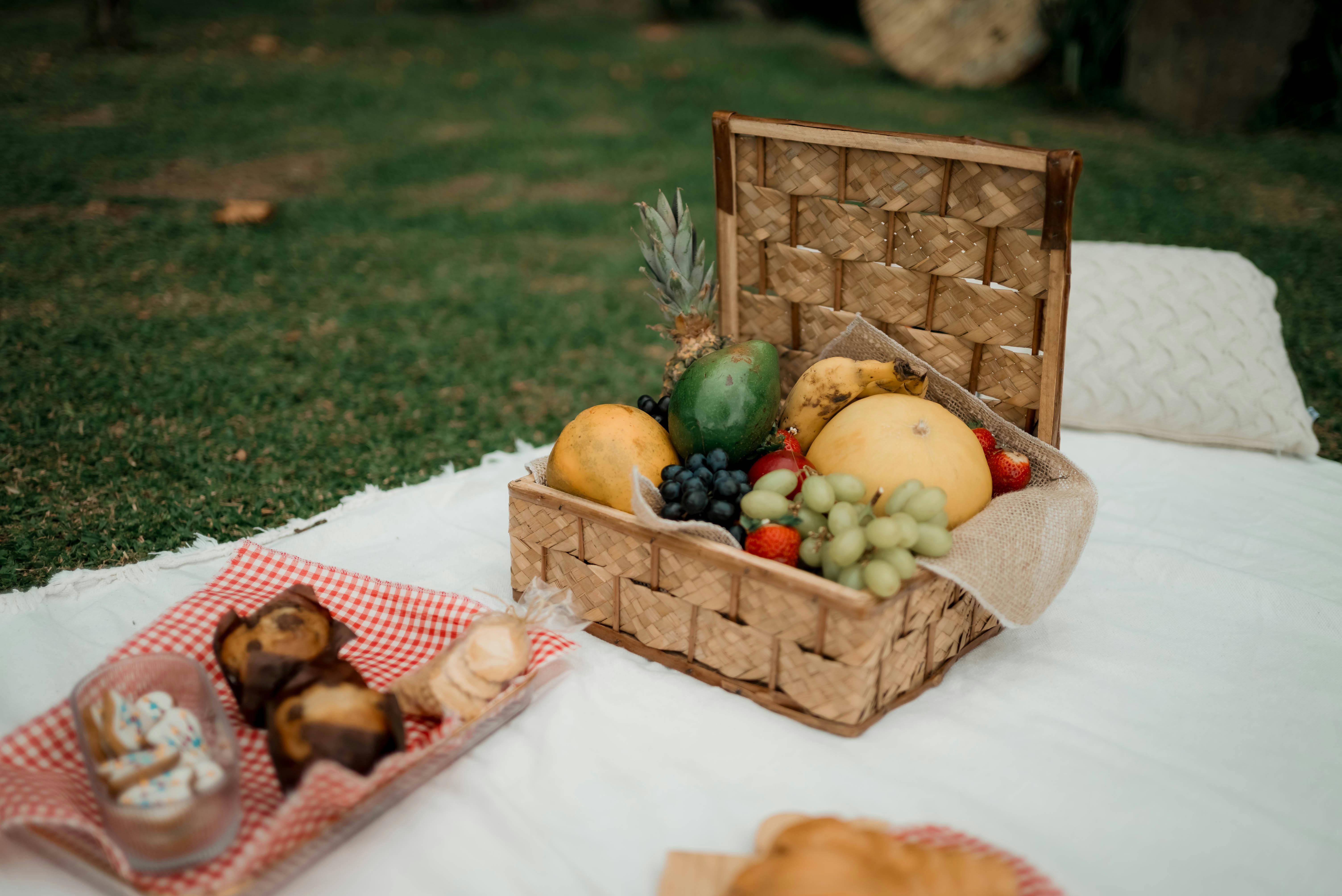 A delightful picnic scene showcasing a fruit basket and pastries on a white blanket outdoors.