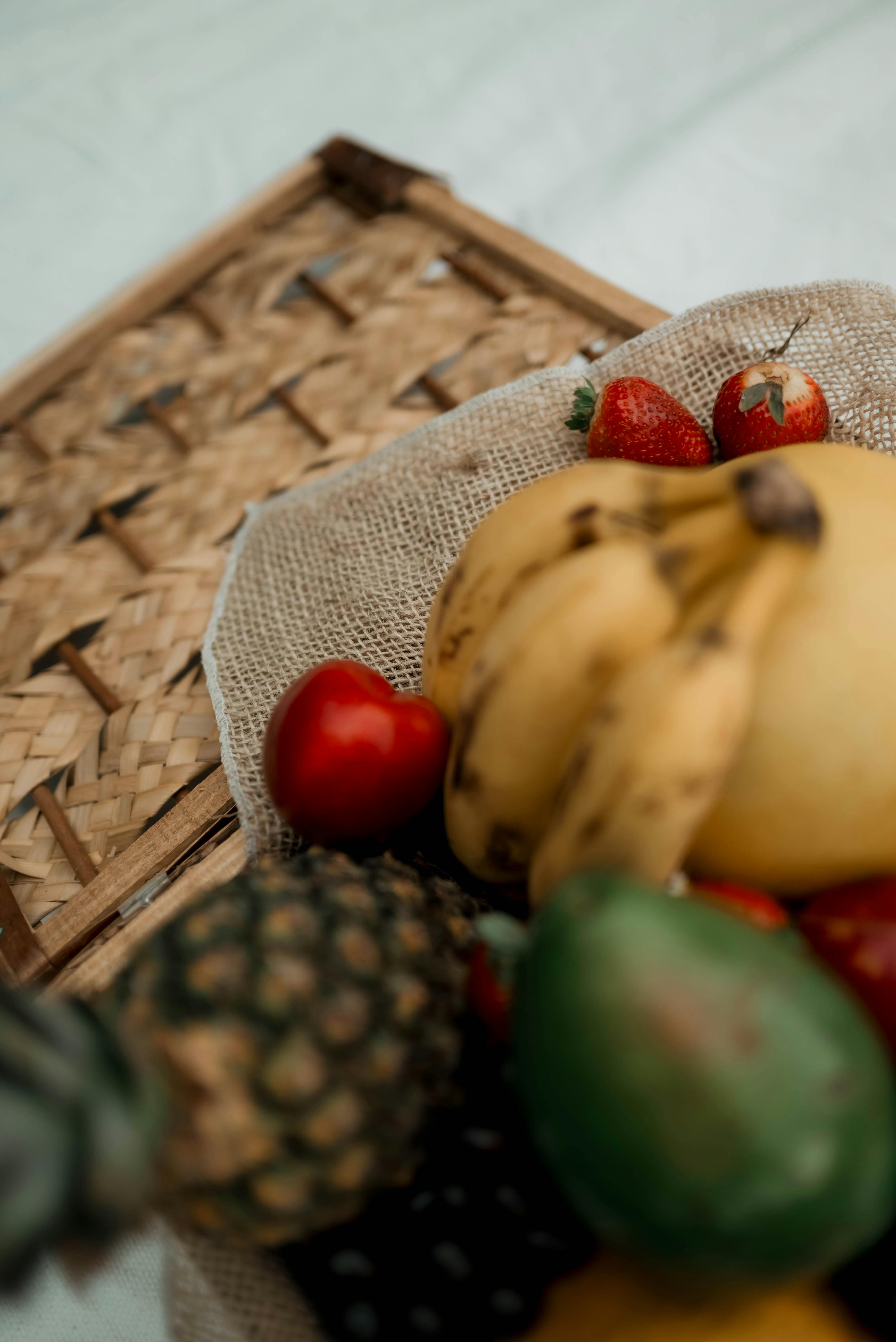 Gratuit Un assortiment vibrant de fruits tropicaux, notamment d'ananas, de banane et de fraise, sur une table tressée. Photos