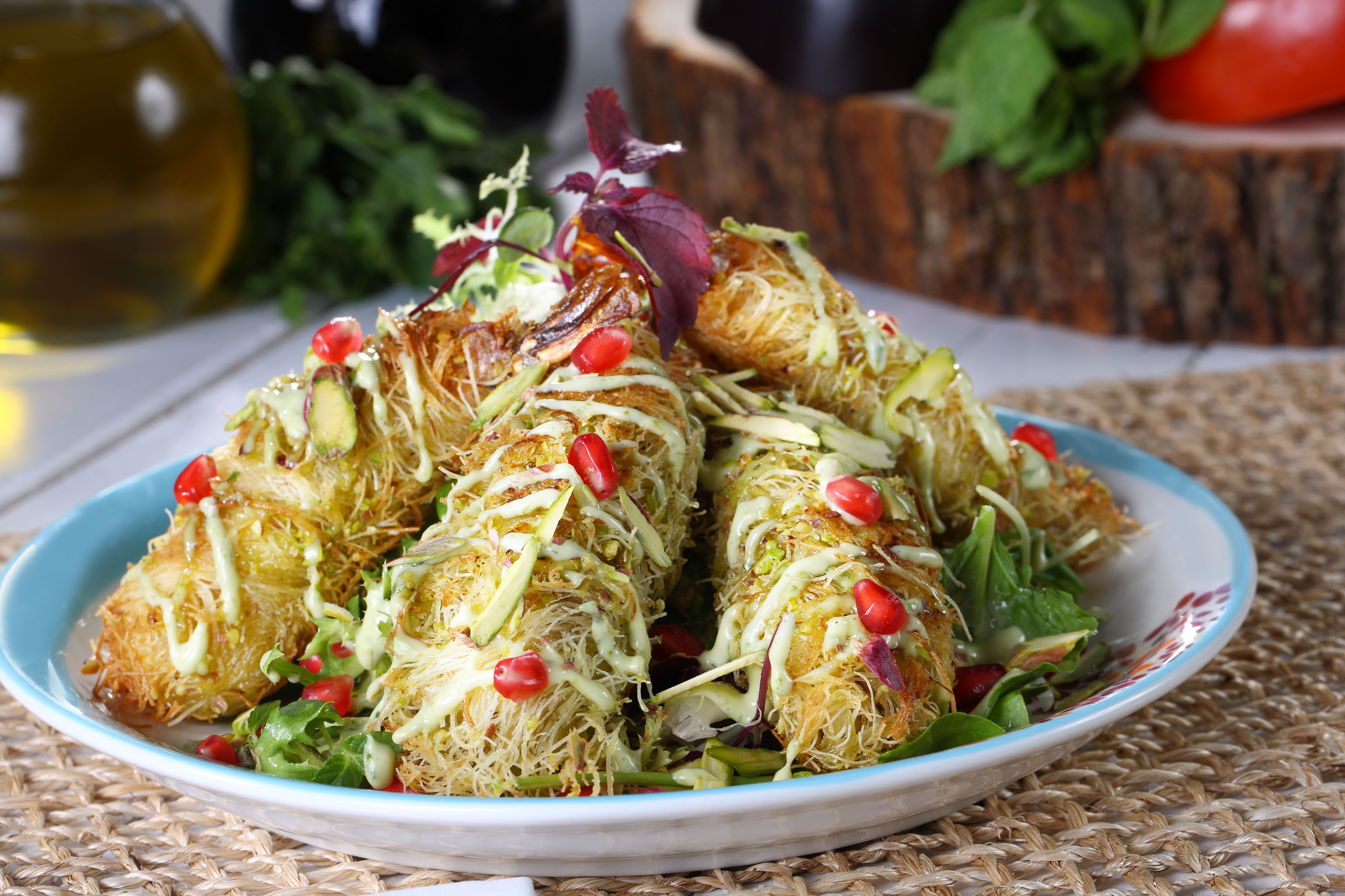 Flavorful Lebanese Kanafeh topped with pistachios and pomegranate seeds, garnished with fresh greens.
