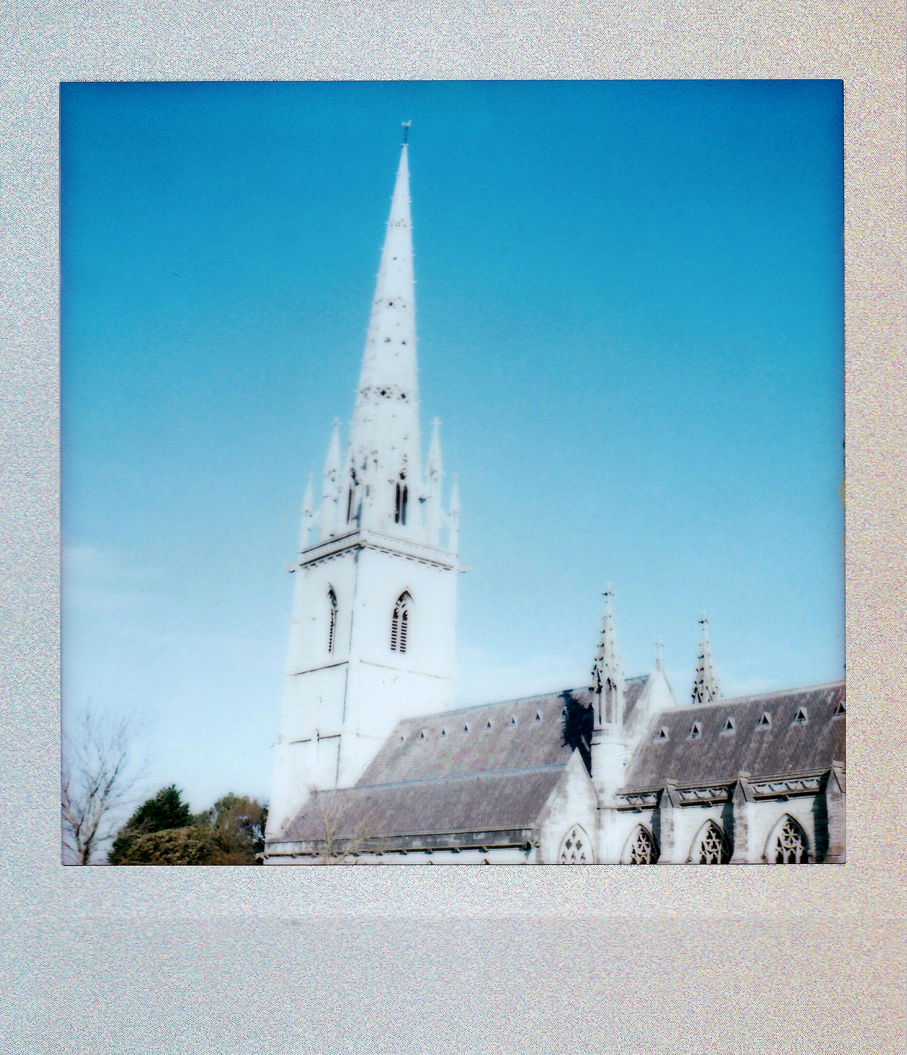 Polaroid of a Gothic church spire with a clear blue sky background, capturing architectural elegance.