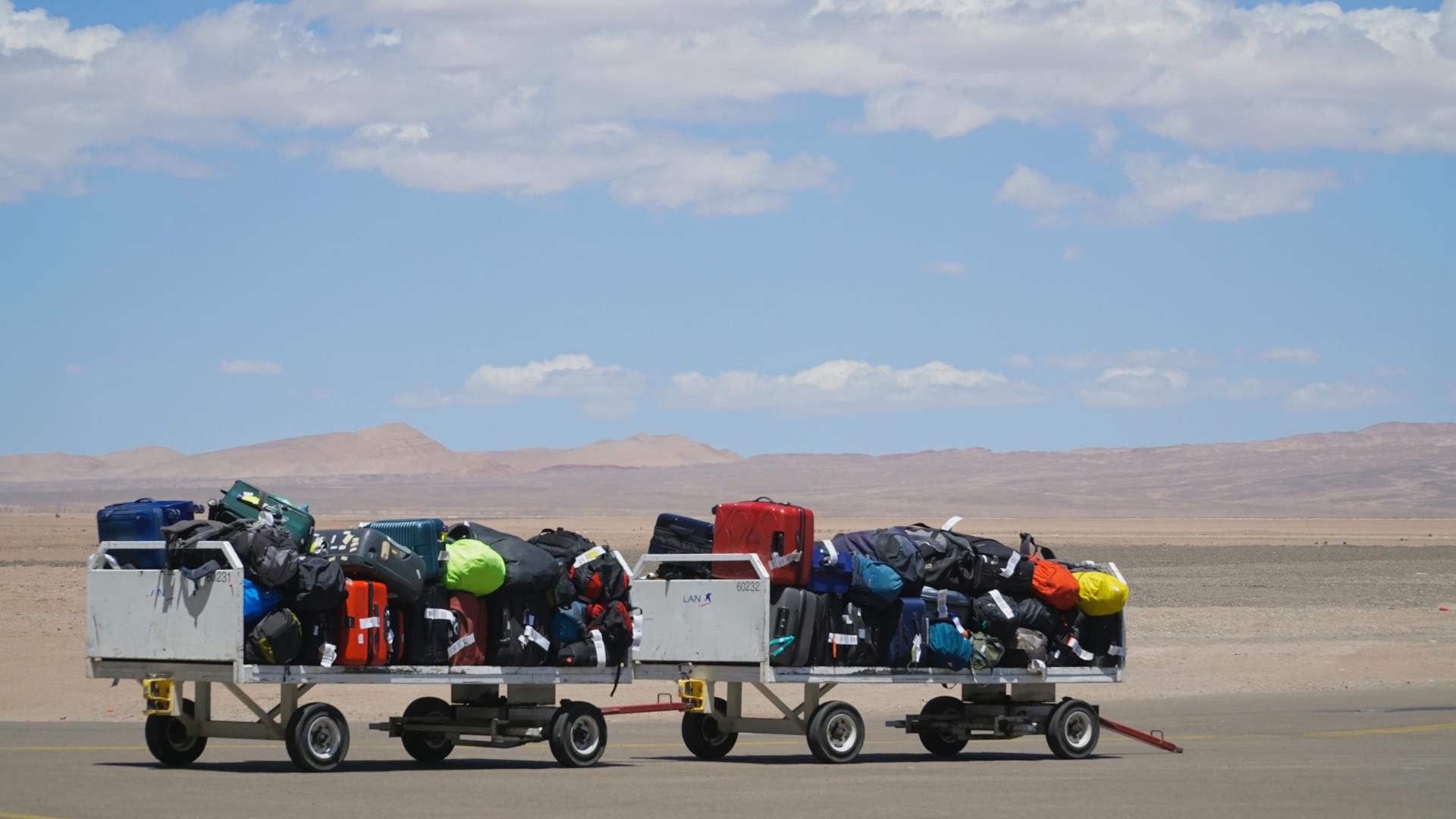 Luggage carts at airport loaded with colorful bags under clear sky. Outdoor travel scene.