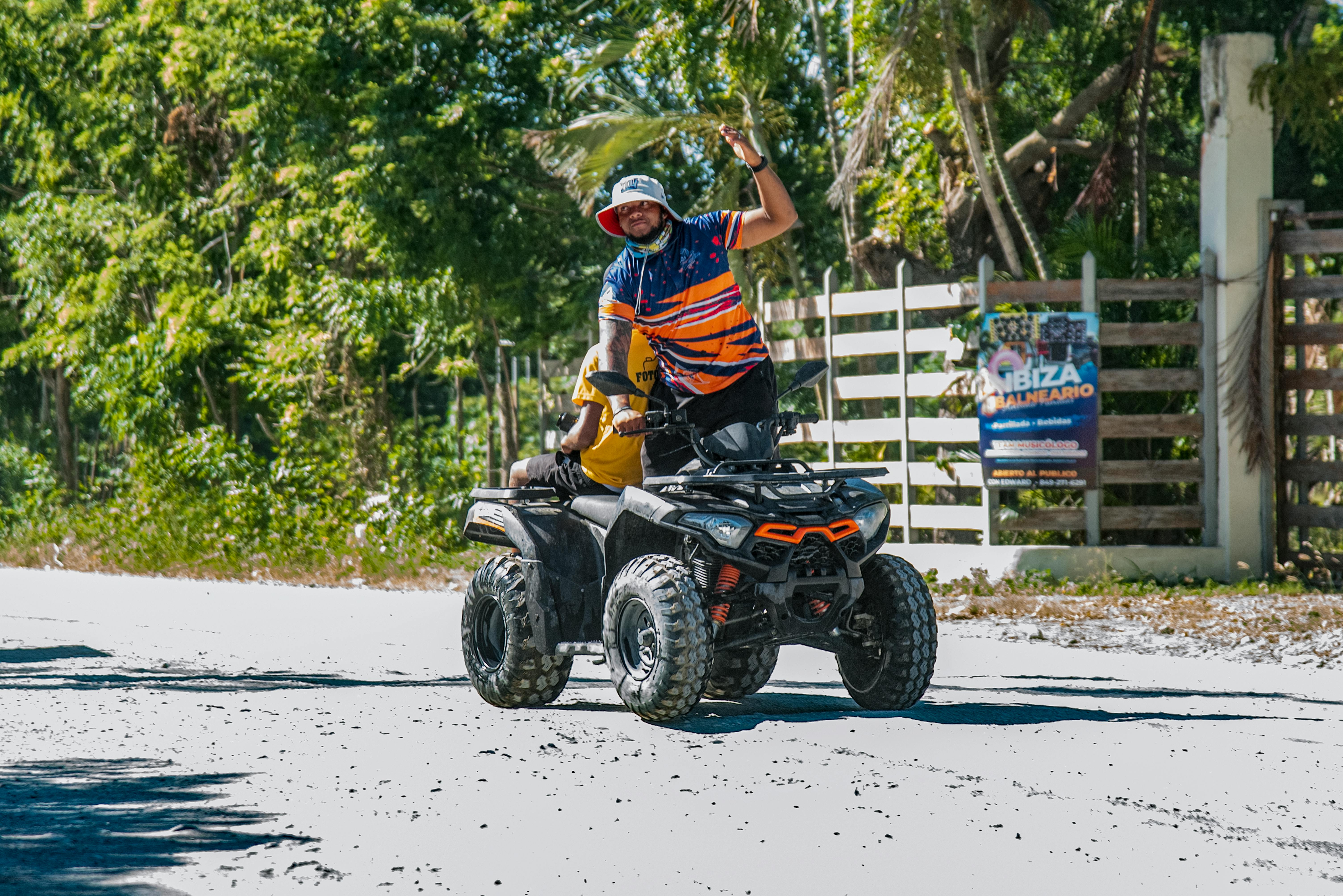 A person riding an ATV on a sunny road surrounded by lush greenery.