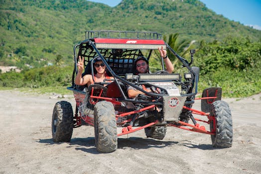 Two adults enjoy an off-road buggy ride in a scenic setting with natural greenery.