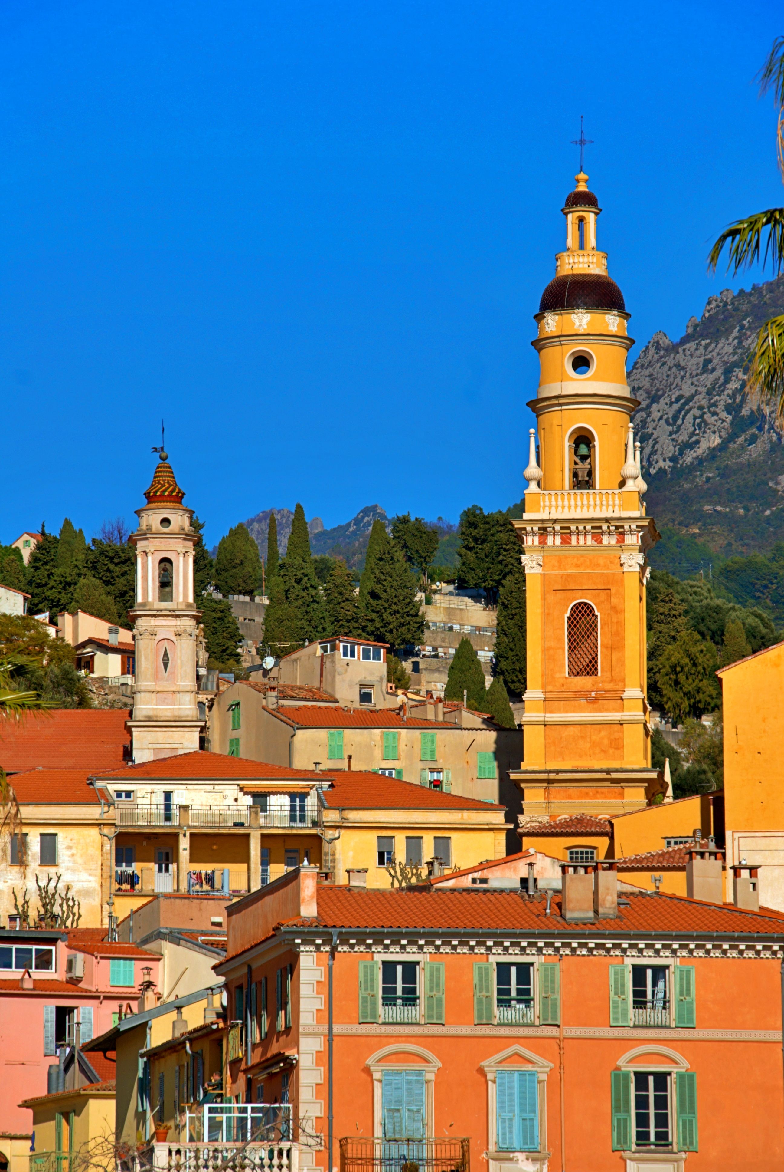 Colorful buildings and bell towers in Menton, France under a clear blue sky.