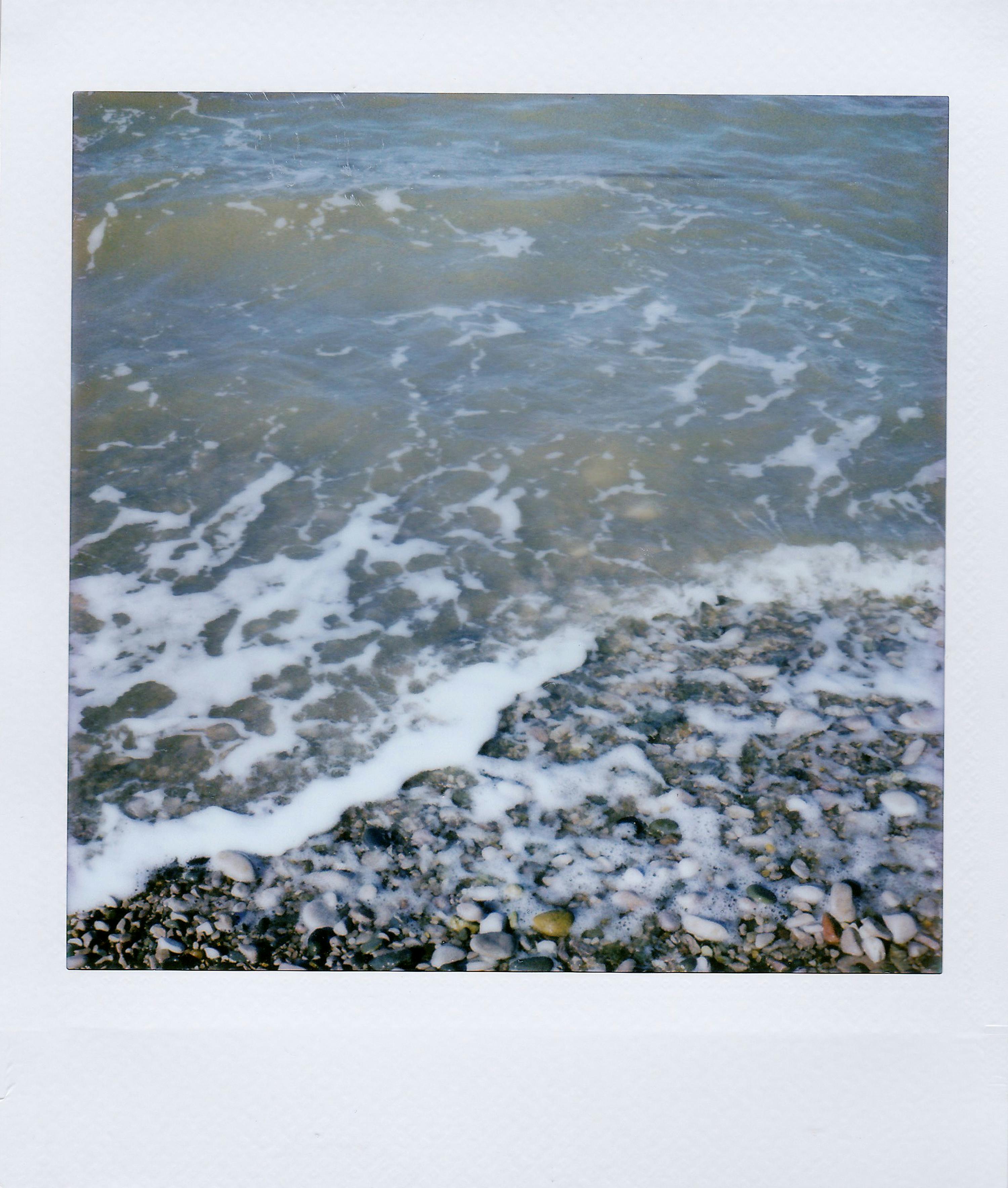 Polaroid image of a tranquil pebble beach with gentle waves lapping at the shore.