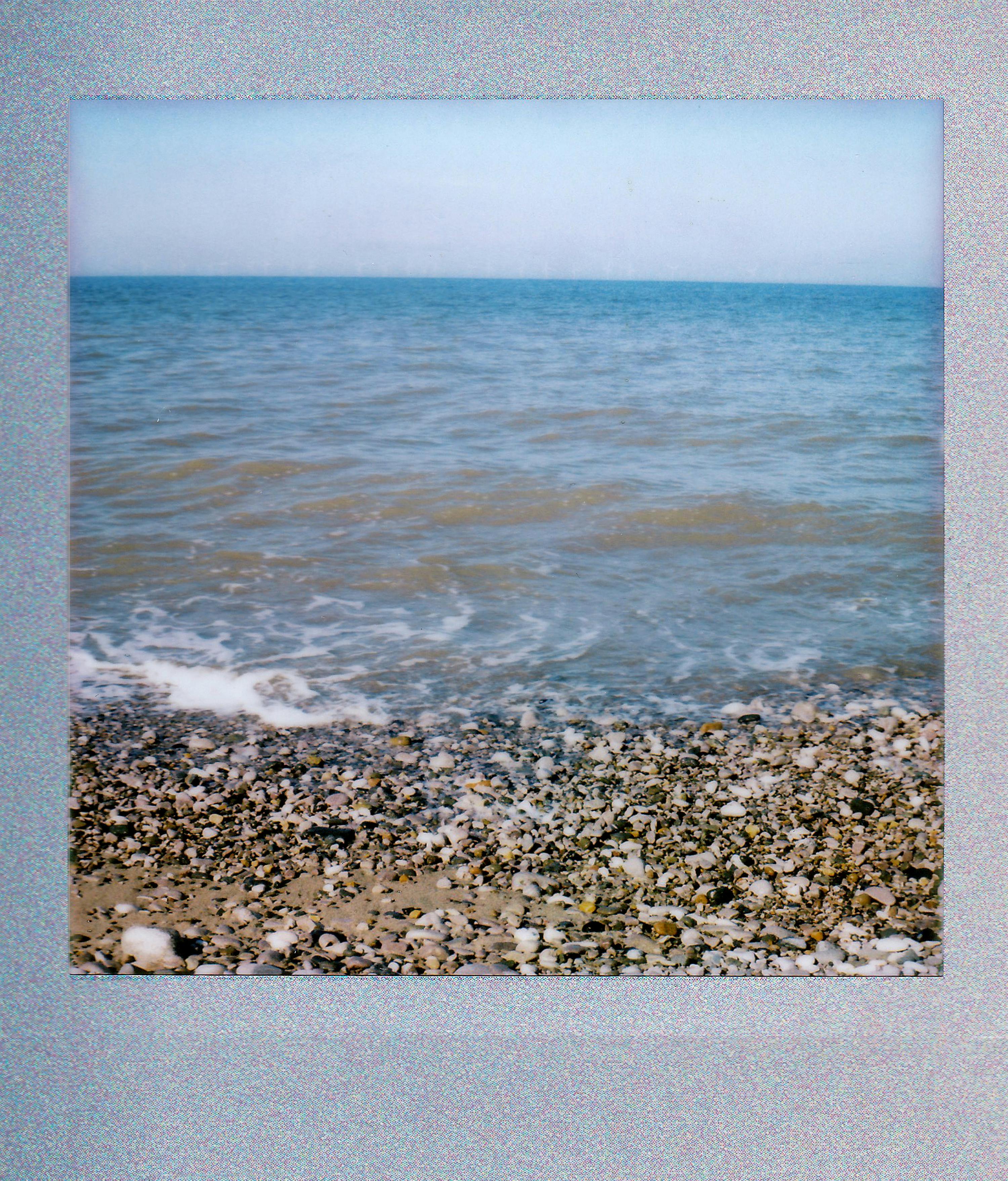 A vintage-style polaroid of a scenic pebble beach with gentle waves, evoking a timeless summer feel.
