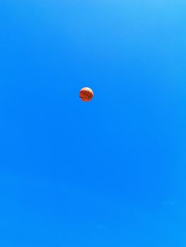 A basketball soaring in the sky against a bright blue backdrop, creating a dynamic and vibrant scene.