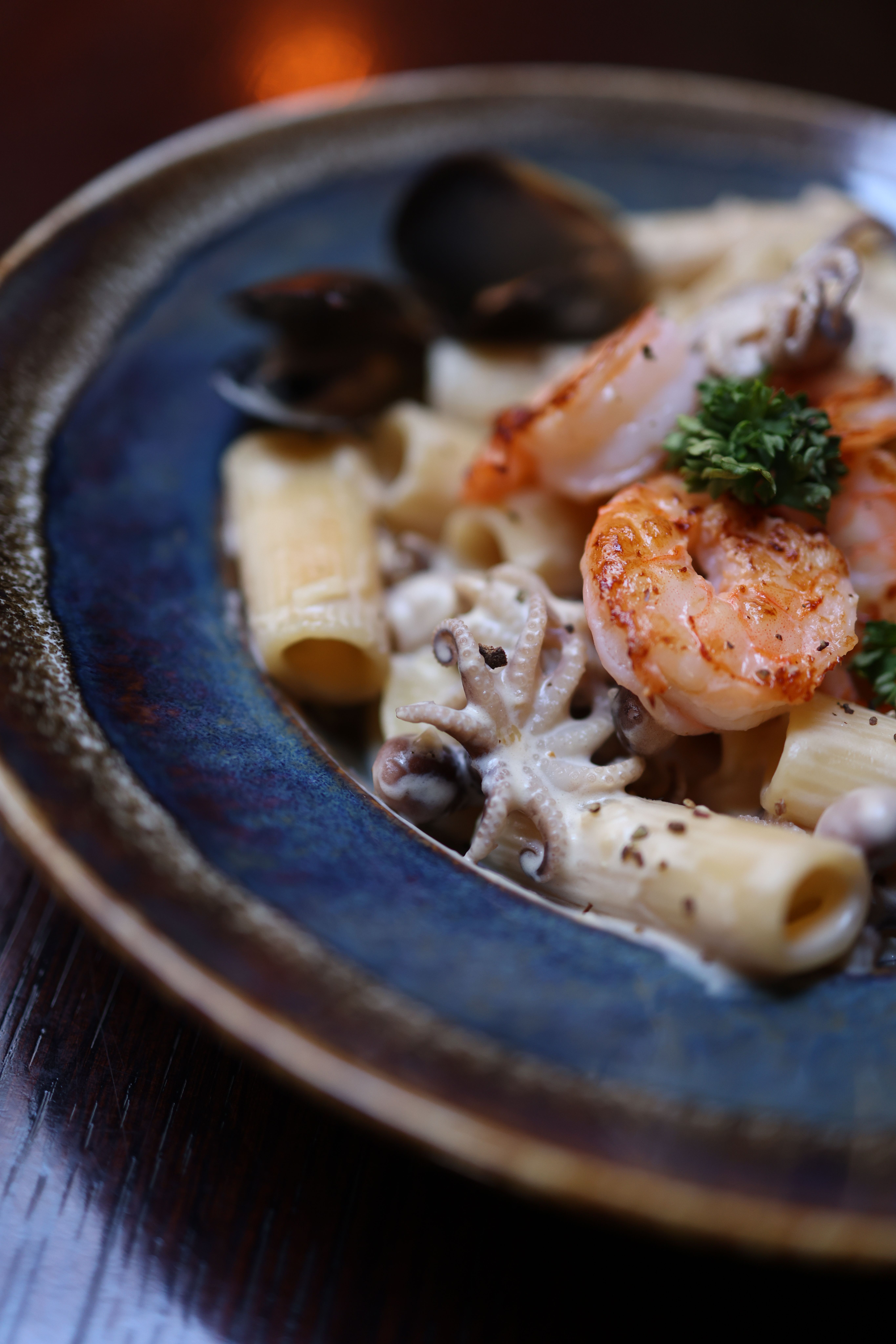 Close-up of seafood pasta with shrimp and mushrooms on blue plate.