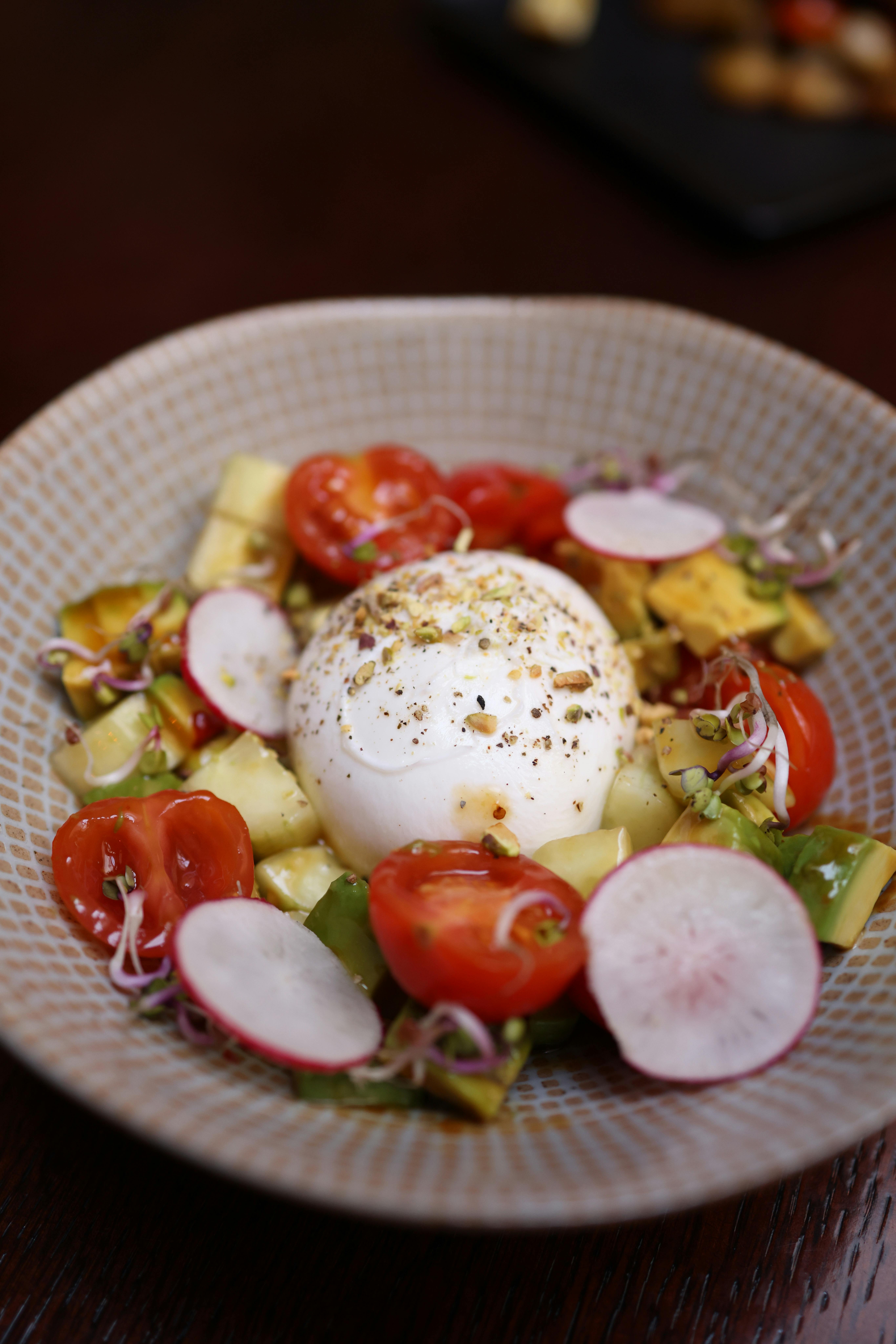 Vibrant burrata salad with heirloom tomatoes, radishes, and avocado, garnished with sprouts.