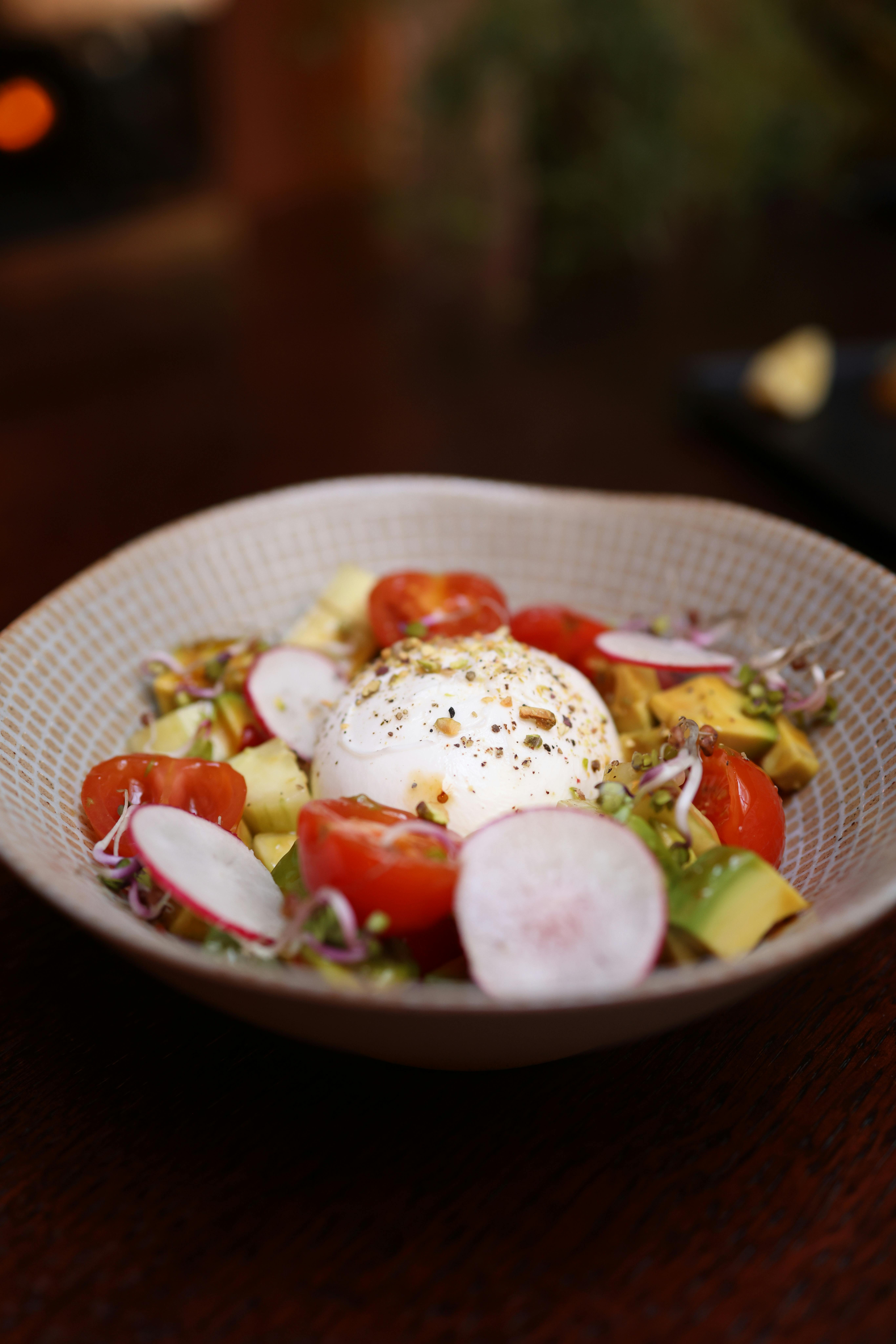 Fresh burrata salad with cherry tomatoes, avocado, and radishes in a ceramic bowl.