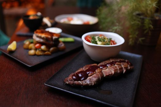 Gourmet steak with sauce and sides on a dark plate, showcasing fine dining ambiance.