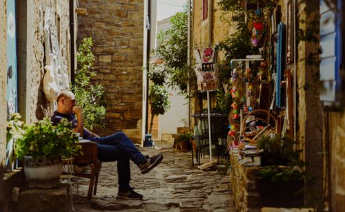 Free Man relaxing in charming stone alleyway of an old European village, surrounded by plants and crafts. Stock Photo