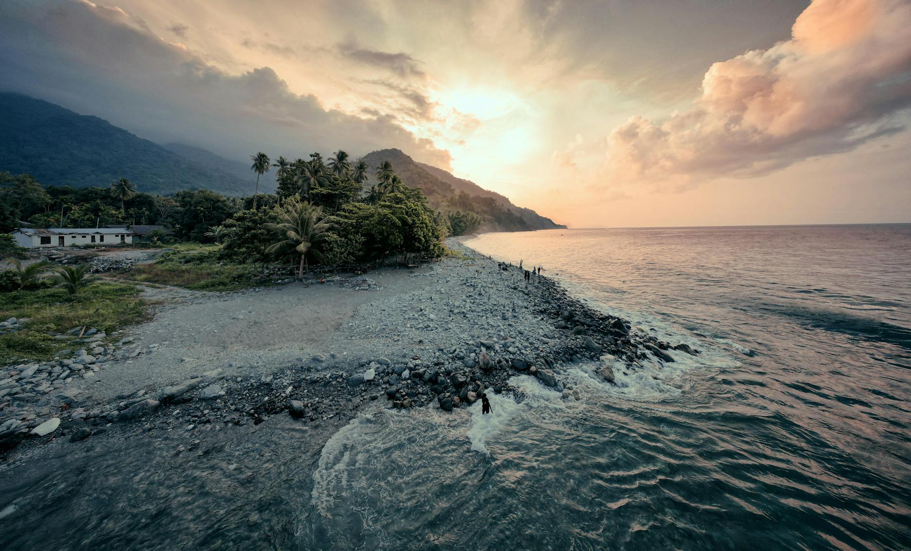 Tranquil coastal view featuring waves, lush greenery, and a vibrant sunset sky.