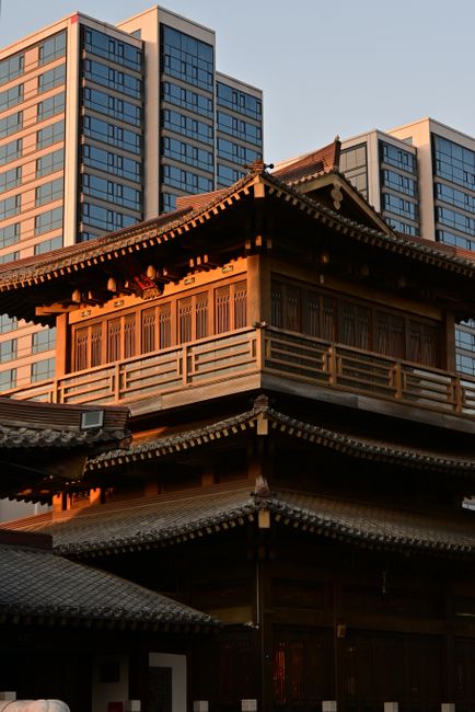 A traditional Chinese building contrasted with modern skyscrapers at sunset.