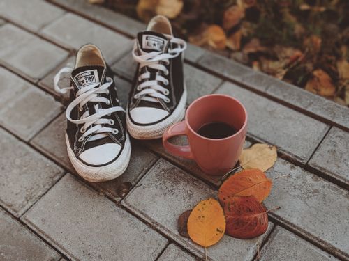 Free Black sneakers and a pink coffee mug on a stone pavement surrounded by autumn leaves. Stock Photo