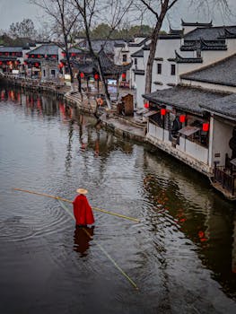 A person in traditional attire rows a boat in a historic Chinese water town, showcasing cultural heritage.