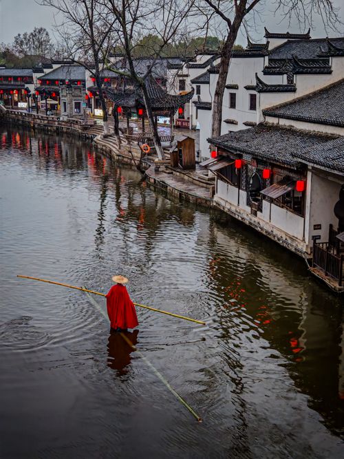 Free A person in traditional attire rows a boat in a historic Chinese water town, showcasing cultural heritage. Stock Photo
