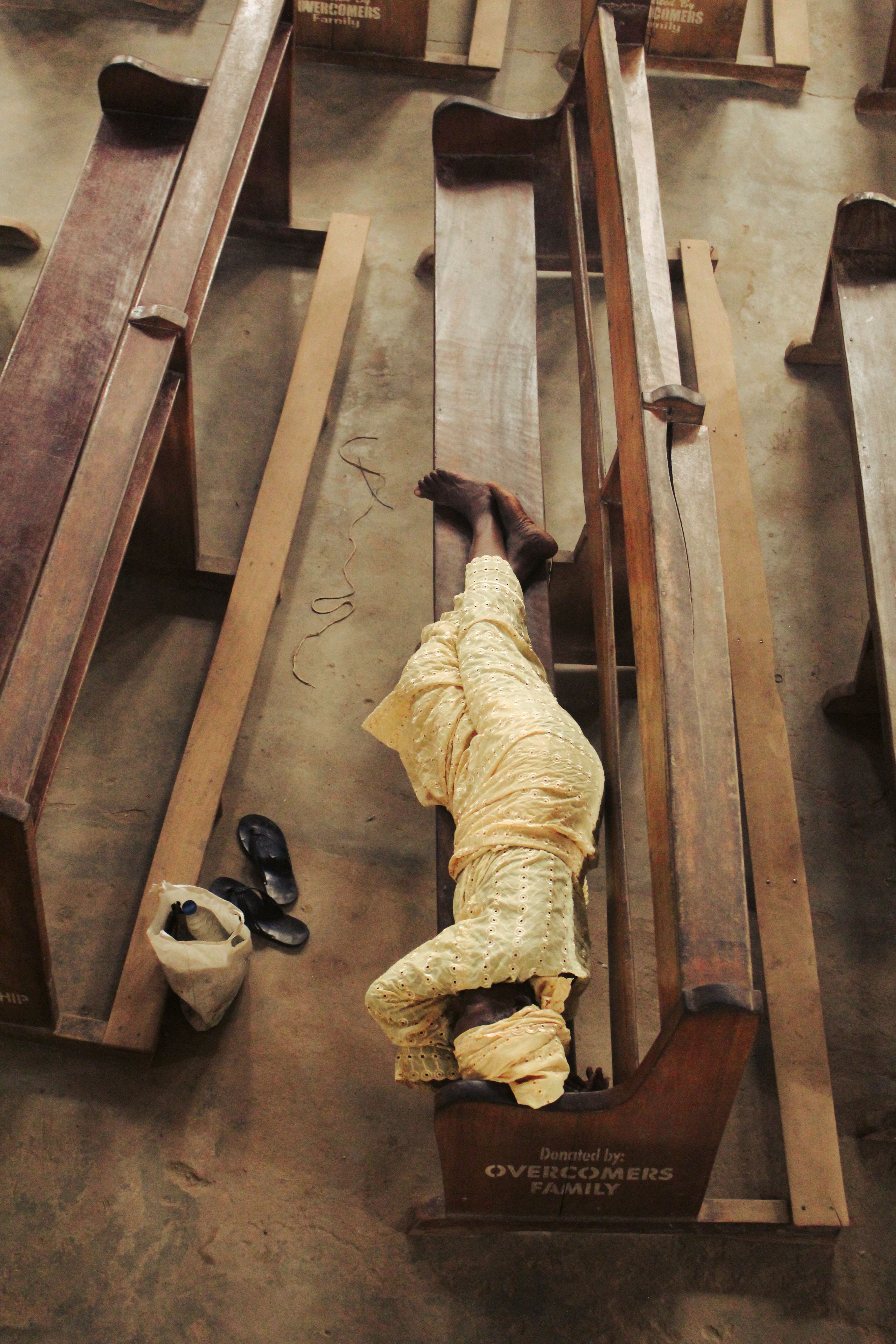 Top-down view of a person resting on church pews in Amechi, Nigeria.