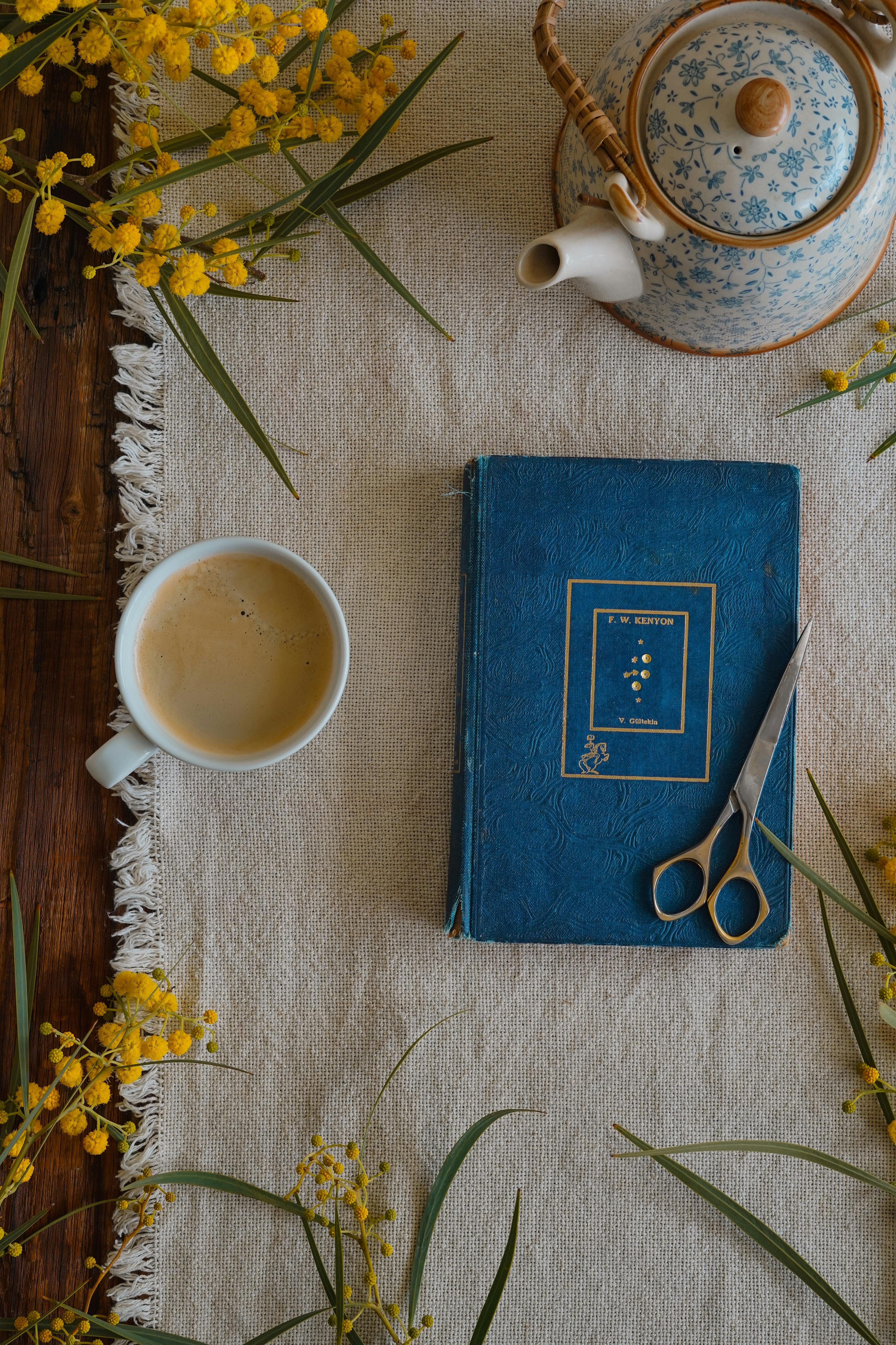 A cozy flat lay of a tea setting with a vintage book, surrounded by vibrant yellow flowers.